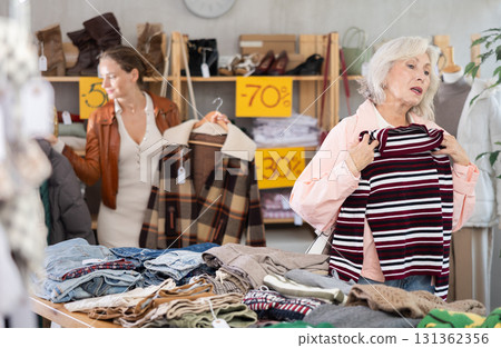 Elderly woman choosing sweaters against the background of female buyer Elderly woman choosing sweaters against the background of female buyer 131362356