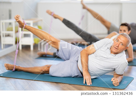 Pilates class for seniors - group of seniors doing leg stretches using resistance bands 131362436