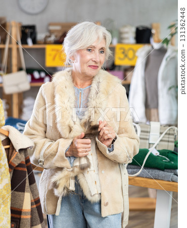 Senior woman chooses and try on fur jacket in store 131362448