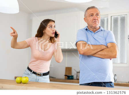 Adult daughter, talking on a mobile phone, is trying to prove her case to a frustrated father Adult daughter, talking on a mobile phone, is trying to prove her case to a frustrated father 131362576
