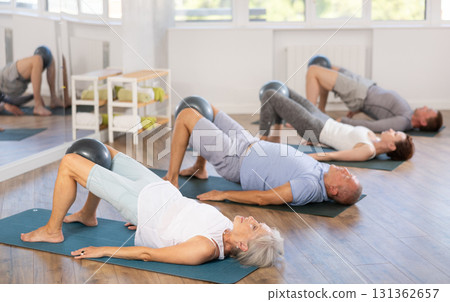 Elderly woman performs glute bridge with softball in knees 131362657