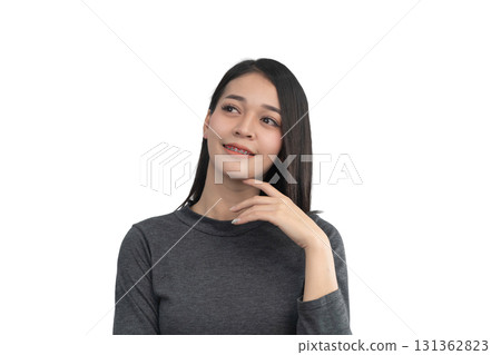 Thoughtful young woman in casual clothing with long black hair, smiling and posing against a white background, showcasing a joyful candid moment of reflection. Thoughtful young woman in casual clothing with long black hair, smiling and posing against a white background, showcasing a joyful candid moment of reflection. 131362823