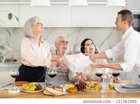 Young man handing a gift to senior woman sitting around table 131362868