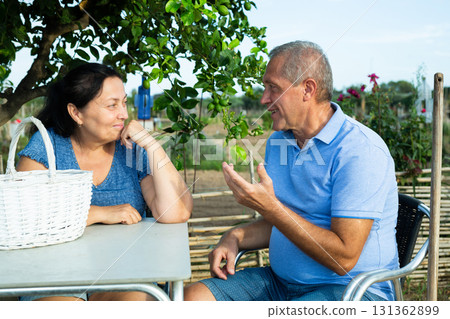 Happy married couple sitting at table and talking after gardening Happy married couple sitting at table and talking after gardening 131362899