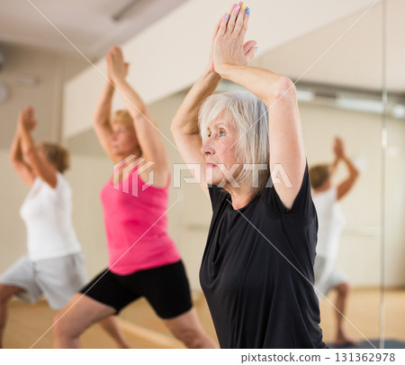 Aged woman performing Anjaneyasana during group yoga training Aged woman performing Anjaneyasana during group yoga training 131362978