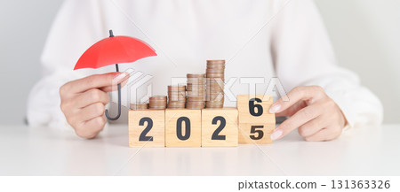 2025 end year to Happy New Year 2026 with hand holding red umbrella and money stack growing. Insurance, protection, safety and New year holiday Concepts 131363326