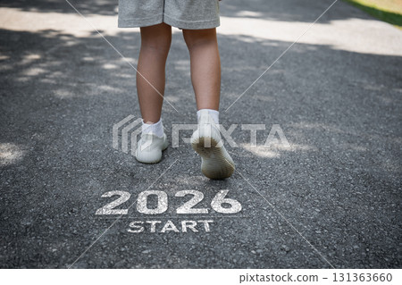 Young child walking towards the future with determination on a path marked 2026 signifying new beginnings and goals to achieve ahead in life. 131363660