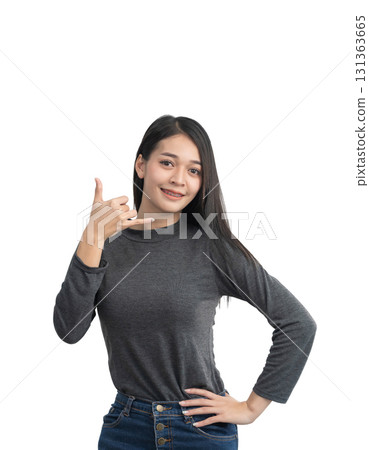 Young woman making the 'shaka' sign with a friendly smile, showcasing positivity and relaxed attitude in a casual outfit against a white background 131363665