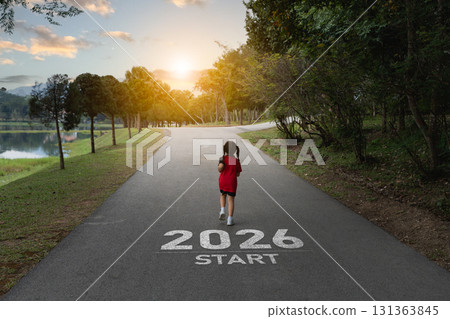 Young girl running towards a bright future on a scenic path marked 2026 start with serene nature backdrop and soft golden sun rays illuminating the scene 131363845