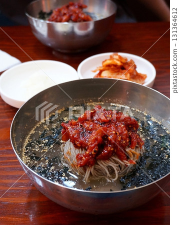 Naengmyeon, a refreshing Korean cold noodle dish served in an icy broth, topped with sliced vegetables, a boiled egg, and spicy sauce. Perfect for summer food photography and Korean cuisine projects. 131364612