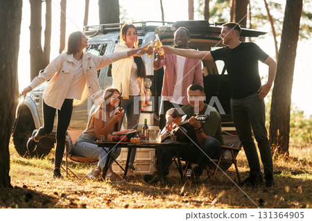 Making cheers with beer bottles. Group of friends are having fun together in the forest Making cheers with beer bottles. Group of friends are having fun together in the forest 131364905