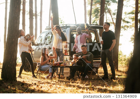Near the car that is parked behind them. Group of friends are having fun together in the forest Near the car that is parked behind them. Group of friends are having fun together in the forest 131364909