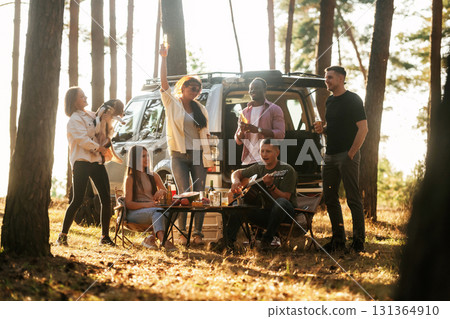 Near the car that is parked behind them. Group of friends are having fun together in the forest Near the car that is parked behind them. Group of friends are having fun together in the forest 131364910