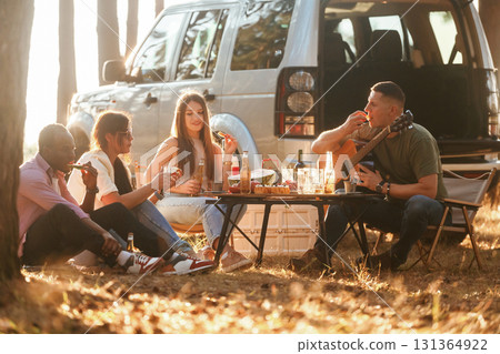 Near the car that is parked behind them. Group of friends are having fun together in the forest Near the car that is parked behind them. Group of friends are having fun together in the forest 131364922