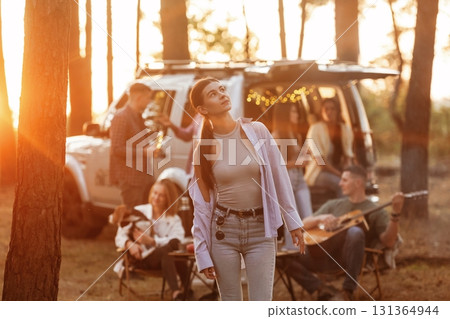 Girl in casual clothes is standing and posing. Group of friends are having fun together in the forest Girl in casual clothes is standing and posing. Group of friends are having fun together in the forest 131364944