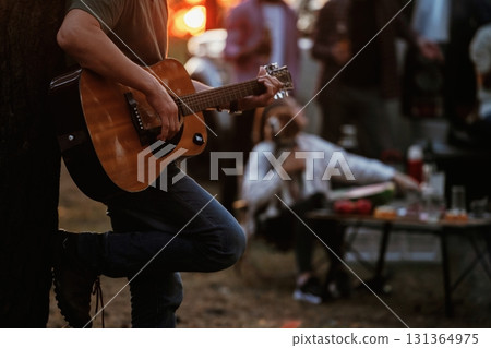 Guy is playing acoustic guitar. Group of friends are having fun together in the forest 131364975