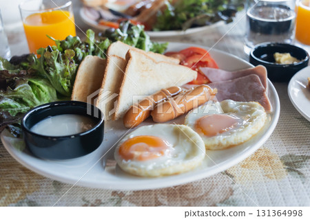 Breakfast Plate with Eggs, Ham, Sausages, Toast, Fresh Vegetables and Juice on a Table for a Delicious Morning Meal Breakfast Plate with Eggs, Ham, Sausages, Toast, Fresh Vegetables and Juice on a Table for a Delicious Morning Meal 131364998