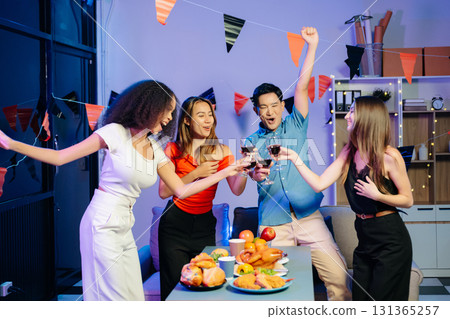 Friends celebrate indoors with food and wine, sharing laughs and toasts at a festive gathering. Friends celebrate indoors with food and wine, sharing laughs and toasts at a festive gathering. 131365257