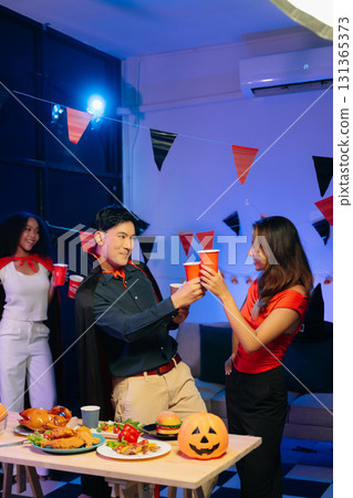 Joyful friends in vibrant Halloween costumes share drinks and laughter at a festive indoor party. 131365373