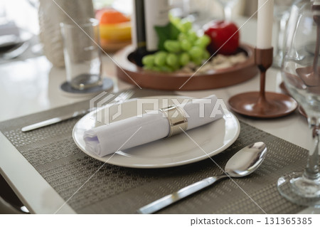 Elegant dining table setting with refined tableware, neatly arranged napkin, wine bottle, fresh fruits, and decorative elements for special occasions 131365385