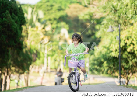 Young girl riding bicycle in park on sunny day, joyful expression, surrounded by greenery, nature, outdoor activity, childhood adventure, playful spirit Young girl riding bicycle in park on sunny day, joyful expression, surrounded by greenery, nature, outdoor activity, childhood adventure, playful spirit 131366312