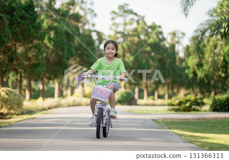 Happy young girl riding bicycle in park during sunny day, enjoying childhood and outdoor activities in nature, healthy lifestyle and joy of movement Happy young girl riding bicycle in park during sunny day, enjoying childhood and outdoor activities in nature, healthy lifestyle and joy of movement 131366313