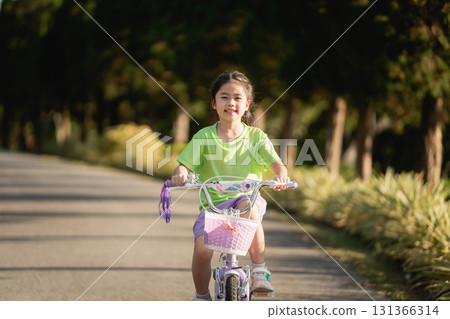 Young girl riding a bicycle on a sunny day in a peaceful park, enjoying outdoor activity and the joy of childhood in a vibrant natural setting Young girl riding a bicycle on a sunny day in a peaceful park, enjoying outdoor activity and the joy of childhood in a vibrant natural setting 131366314