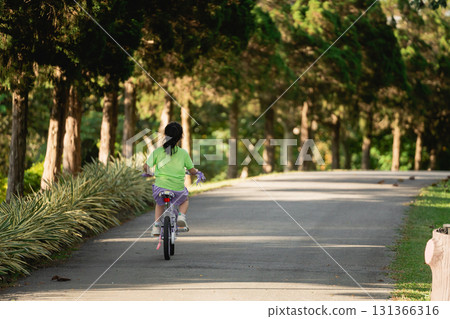 Child Riding Bicycle on a Tree-Lined Pathway in a Bright Green Park During Sunny Day, Outdoor Fun and Adventure for Kids Child Riding Bicycle on a Tree-Lined Pathway in a Bright Green Park During Sunny Day, Outdoor Fun and Adventure for Kids 131366316