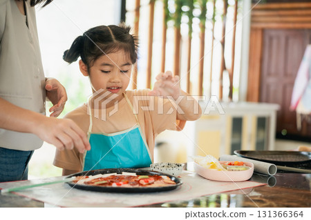 Young girl preparing homemade pizza in a kitchen with parents, focusing on creativity and joy of cooking together with fresh ingredients and teamwork Young girl preparing homemade pizza in a kitchen with parents, focusing on creativity and joy of cooking together with fresh ingredients and teamwork 131366364