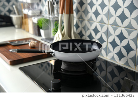 Modern kitchen scene with a white and black non-stick frying pan on a gas stove. 131366422