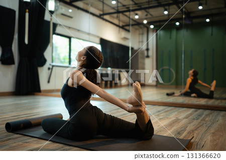 Female yogi in black outfit doing a backbend stretch pose in a spacious studio 131366620