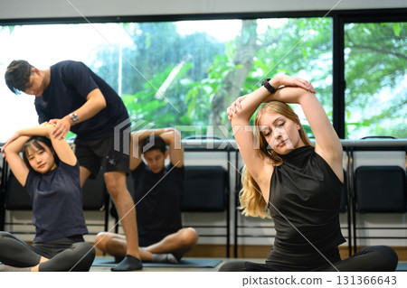 Diverse group practicing seated arm stretches during yoga session in a bright studio 131366643