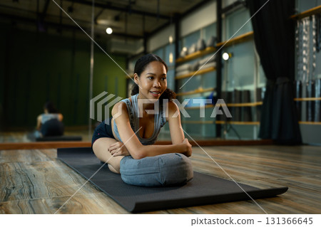 Calm female in sportswear performing relaxing yoga pose on mat using a cushion in a modern studio Calm female in sportswear performing relaxing yoga pose on mat using a cushion in a modern studio 131366645