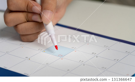 Hand holding pen, pointing to a date on a calendar, symbolizing scheduling, and planning 131366647