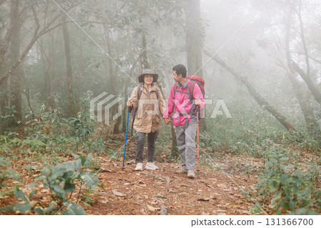 Two hikers walking together on forest trail in foggy weather with backpacks and trekking poles, symbol of adventure, teamwork, outdoor lifestyle, exploration, journey and travel inspiration. Two hikers walking together on forest trail in foggy weather with backpacks and trekking poles, symbol of adventure, teamwork, outdoor lifestyle, exploration, journey and travel inspiration. 131366700