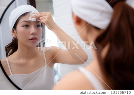 Beautiful young asian woman gently clean on face while looking mirror in bathroom. 131366710