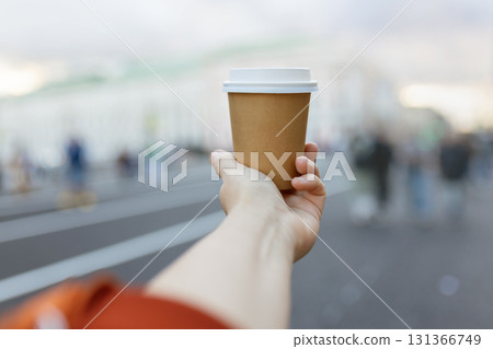 Brown paper cup of drink in women's hand on city street 131366749