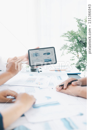 Business data analysis concept with colleagues reviewing financial report on tablet, pointing at chart with growth graph, teamwork discussing statistics, planning strategy and corporate success. 131366843