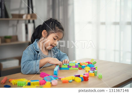 Young Girl Engaged in Creative Play with Colorful Building Blocks at Home in Natural Light, Focused on Developing Skills and Imagination 131367146