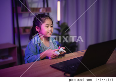 Happy child engaged in gaming activity in cozy indoor setting with colorful neon lights, wearing denim jacket and holding game controller, focused expression on face 131367151