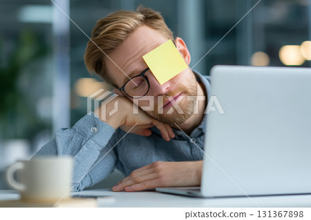 Sleepy man office glasses sticky note on face laptop tired workspace casual stress fatigue funny modern 131367898