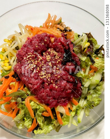 Yukhoe bibimbap with fresh veggies, rice, seasoned raw beef, raw egg yolk, and gochujang. offering a bold mix of flavors and textures in a classic Korean dish. 131368098