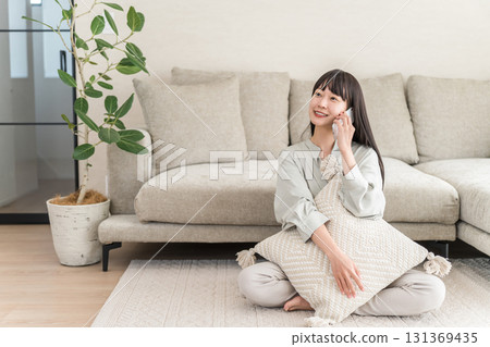 Japanese woman calling on smartphone (home, living room, smiling) 131369435