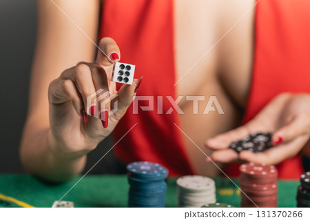 Stylish Woman Playing Poker with Poker Chips and Dice, Focus on Hand Holding Dice, Gambling Theme in Luxurious Casino Environment 131370266