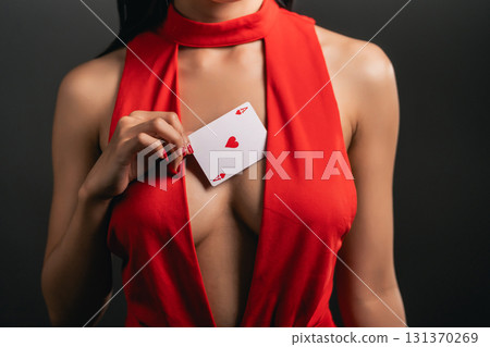 Elegant woman in a red dress revealing a playing card with a heart symbol, representing love and passion in a stylish and captivating way 131370269