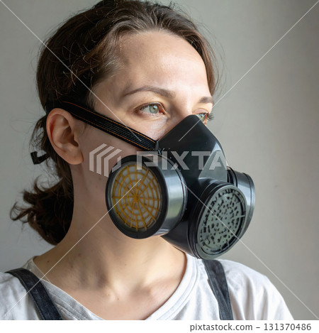 Woman wearing black gas mask looking away from window Woman wearing black gas mask looking away from window 131370486