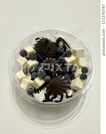 Swirled yogurt ice cream dessert served in a cup, smooth creamy texture with glossy surface, topped with fresh fruit pieces, highlighting its refreshing and inviting appearance in detail 131370747