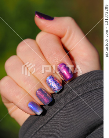 Multicolored manicure in bright sunlight. Skittles nails with many textures. Colorful shiny manicure with different textures in purple and violet colors over street background. Eye-catching nail art 131372299
