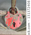 A heart-shaped lock, painted in a faded red color, is fixed on the old, rusty bridge railing. The lock shows signs of wear and tear, indicating its durability. It is a symbol of eternal love. 131372408