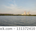Modern thermal power plant towers on the shore of the Gulf of Finland. The industrial towers emit steam, with a backdrop of greenery, water, and a clear sky. 131372410